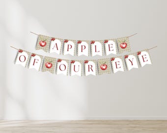 Può includere: Un banner con la scritta "APPLE OF OUR EYE" in lettere rosse. Ogni gagliardetto ha uno sfondo bianco con un'illustrazione di una mela rossa. Il banner è appeso a un filo sottile e marrone.