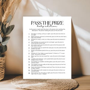 Peut inclure: Une carte blanche imprimée avec le jeu "PASS THE PRIZE baby edition" et des instructions pour un jeu de baby shower. La carte est posée sur un fond neutre avec des plantes décoratives.