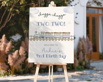 May include: A wooden easel displays a sign with a train illustration and the text "chugga chugga TWO TWO!" and "Welcome to Arhie's 2nd Birthday" in blue. The sign is set outdoors.