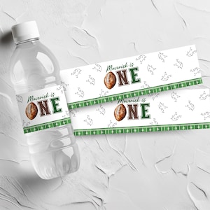 May include: A clear plastic water bottle with a white cap and a label that reads "Maverick is ONE" with a football graphic. Two matching labels are next to the bottle. The labels have a football theme.