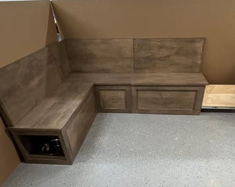 May include: A wooden corner bench with a dark stain finish. The bench has a backrest and a storage compartment. A pull-out drawer is visible on the right side. The bench is designed for indoor use.