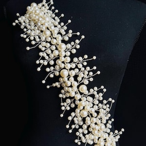 Può includere: Un accessorio per capelli da sposa con grappoli di perle finte di varie dimensioni, attaccate a delicati rami di filo argentato. Il design è presentato su uno sfondo nero, mostrando i dettagli intricati e lo stile elegante del copricapo.