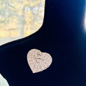 May include: A sparkling heart-shaped brooch, densely covered in small, clear rhinestones. The brooch is pinned to a black fabric surface, creating a contrast that highlights the brilliance of the crystals. The brooch is a fashion accessory.