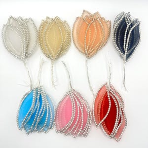 May include: Seven decorative flower ornaments in various colors, including white, yellow, orange, navy, blue, pink, and red. Each flower features a sheer petal design with silver rhinestone accents and a thin wire stem.