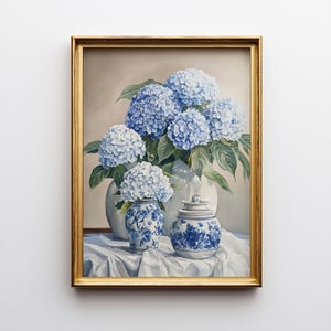 Gold framed hydrangea painting with blue blooms in porcelain jars with chinoiserie pattern against neutral background. Styled for Grandmillennial art aesthetic. New home gift idea art featuring elegant blue hydrangea floral illustration.