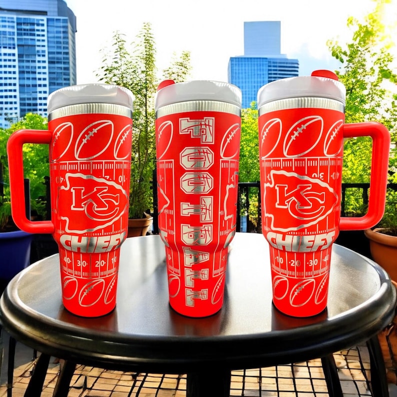 May include: Three red insulated tumblers with white lids and handles. Each tumbler features a football field design with the words "FOOTBALL" and the Kansas City Chiefs logo. The tumblers have measurements in centimetres.
