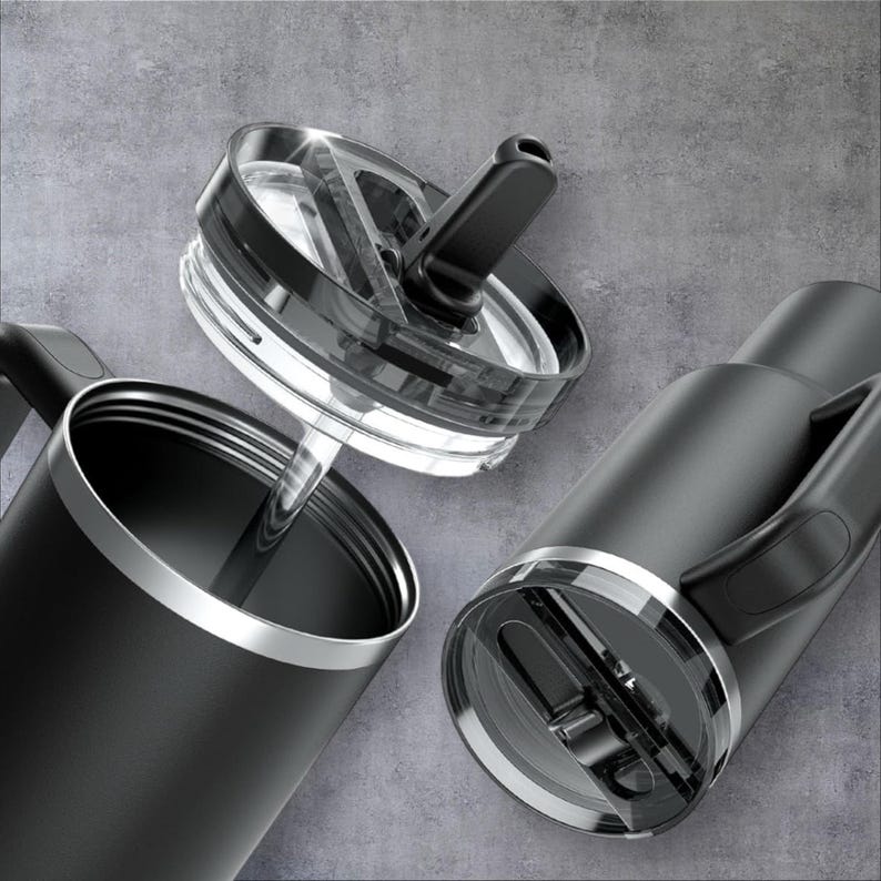 May include: Black insulated travel mug with a handle and a clear lid. The lid has a black flip-top closure and a silver rim. The mug is shown disassembled, with the lid separate from the body. The mug is designed to keep drinks hot or cold.