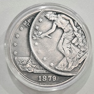Peut inclure: Une pièce de monnaie en argent dans un étui transparent. La pièce représente une femme en robe, tenant une branche, avec l'année 1879. La pièce est ornée d'étoiles et de l'inscription "IN GOD WE TRUST".