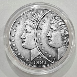 Op de afbeelding: Een zilveren munt uit 1893, in een doorzichtige plastic houder. De munt toont twee profielen van een vrouw, met de inscripties "E PLURIBUS UNUM" en "LIBERTY". De munt is omcirkeld door sterren en een parelrand.