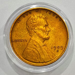 May include: A gold-colored 1909 S Lincoln cent coin, encased in a clear plastic holder. The coin features a profile of Abraham Lincoln, with the words "IN GOD WE TRUST" and "LIBERTY" visible.