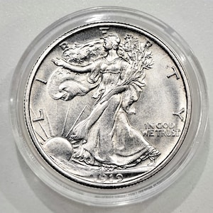 Könnte beinhalten: Eine silberne Walking Liberty Half Dollar Münze, in einer transparenten Schutzhülle. Die Münze zeigt Lady Liberty, die auf die Sonne zugeht und Zweige hält. Die Worte "IN GOD WE TRUST" und das Jahr 1919 sind sichtbar.