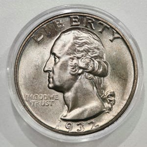 May include: A silver 1932 Washington quarter coin, in a clear protective case. The coin shows a profile of George Washington, with the inscriptions "LIBERTY" and "IN GOD WE TRUST". The year "1932" is displayed at the bottom of the coin.