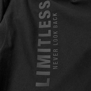May include: Black apparel with the word "LIMITLESS" printed vertically in a dark gray color. Below the word "LIMITLESS" is the phrase "NEVER LOOK BACK" in a dark gray color.