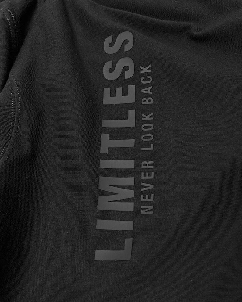 May include: Black apparel with the word "LIMITLESS" printed vertically in a dark gray color. Below the word "LIMITLESS" is the phrase "NEVER LOOK BACK" in a dark gray color.