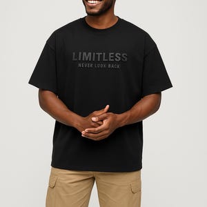 May include: Black crew neck t-shirt with the word "LIMITLESS" and the phrase "NEVER LOOK BACK" printed on the front. The model is wearing khaki cargo pants. The shirt is made of a soft material.