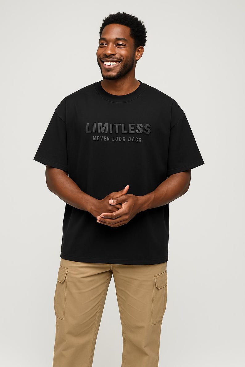 May include: Black crew neck t-shirt with the word "LIMITLESS" and the phrase "NEVER LOOK BACK" printed on the front. The model is wearing khaki cargo pants. The shirt is made of a soft material.