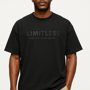 May include: Black crew neck t-shirt with the word "LIMITLESS" embossed across the chest, with the phrase "NEVER LOOK BACK" below. The shirt is worn by a person wearing khaki pants.