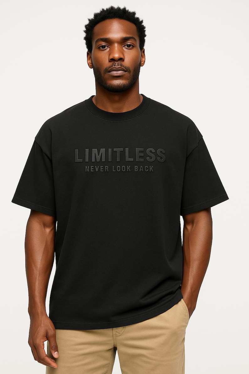 May include: Black crew neck t-shirt with the word "LIMITLESS" embossed across the chest, with the phrase "NEVER LOOK BACK" below. The shirt is worn by a person wearing khaki pants.