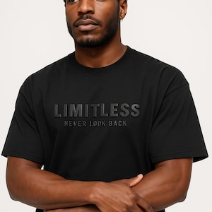 May include: Black crew neck t-shirt with the word "LIMITLESS" embossed across the chest, with the phrase "NEVER LOOK BACK" below. The shirt is a solid black color and has short sleeves.