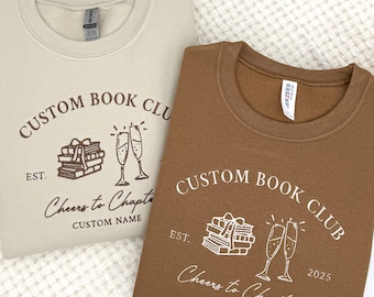 May include: Two brown and beige sweatshirts with a book club design. The design features a stack of books, glasses of champagne, and the text "Custom Book Club" and "Cheers to Chapters".