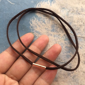 May include: A brown suede cord necklace with a rose gold slider clasp.