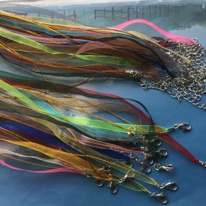 May include: A collection of colorful sheer ribbon necklaces with silver-tone clasps and chain accents. The ribbons are in various colors, including pink, green, blue, and brown, with gold-colored trim. The necklaces are suitable for crafting or jewelry making.