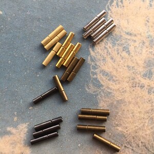 May include: Assortment of metal connector pieces in gold, silver, and black. The pieces are small and cylindrical, with a hole in the center. They are used to connect different parts of jewelry or other crafts.