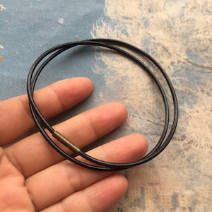 May include: A black cord necklace with a small, gold-toned clasp. The necklace is double-stranded and appears to be made of a thin, flexible material.