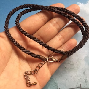 May include: A brown cord necklace with a bronze clasp and extender chain.