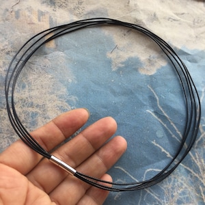 Puede incluir: Un collar negro de múltiples hebras con un cierre plateado.