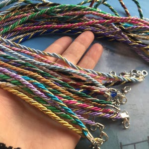 May include: A collection of colorful braided cords with silver clasps. The cords are made of different materials, including silk, cotton, and metallic thread.