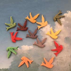 May include: A collection of colorful bird-shaped embellishments in shades of green, red, brown, orange, and yellow. The birds are arranged against a backdrop of a cloudy blue sky, creating a whimsical and decorative effect. These embellishments are ideal for craft projects.