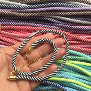 May include: A close-up of a black and white striped cord with gold clasps. The cord is lying on a pile of colorful striped cords.