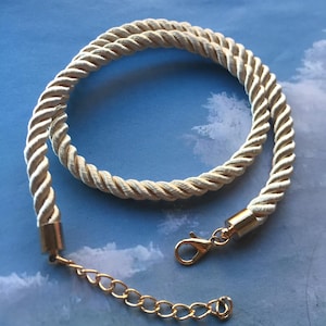 May include: A white rope necklace with a gold clasp and chain. The necklace is made of a thick, braided rope.