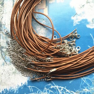 May include: A pile of brown waxed cotton cords with silver lobster clasps. The cords are arranged in a circular pattern.