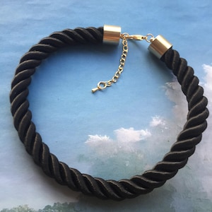 Puede incluir: Un collar gargantilla de cuerda negra con cierres de metal dorado y una cadena extensora.