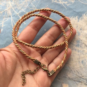 Puede incluir: Un collar de cordón trenzado dorado y marrón con un cierre de bronce.