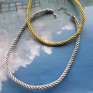 May include: Two rope necklaces, one silver and one gold, on a blue background.