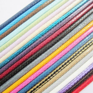 May include: A collection of braided cords in various colours, including blue, red, yellow, white, and black. The cords are arranged in a diagonal pattern, with the ends of the cords overlapping.