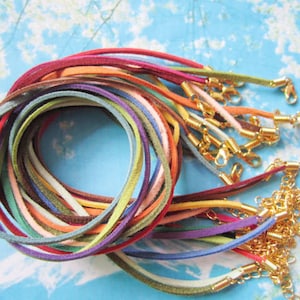 Puede incluir: Un conjunto de cordones de ante de colores con cierres dorados. Los cordones están dispuestos en círculo y están listos para ser utilizados en la elaboración de joyas.