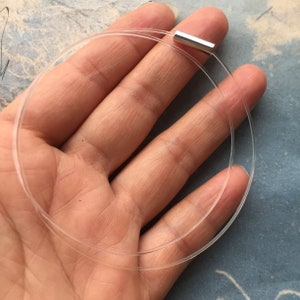 Peut inclure: Un collier fin et flexible transparent avec un fermoir magnétique argenté.
