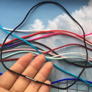 Puede incluir: Una variedad de cordones de algodón encerado en diferentes colores, incluyendo negro, rojo, rosa, azul, verde y blanco. Los cordones están dispuestos en capas, con el cordón negro en la parte superior. Todos los cordones tienen un diámetro de aproximadamente 1 mm.