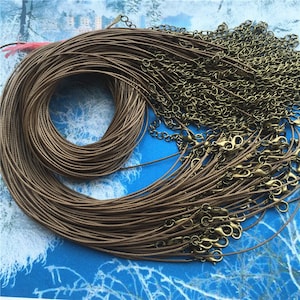 May include: A bulk pack of brown waxed cotton cord, with gold-toned metal clasps. The cord is wound into a coil and the clasps are scattered around it.