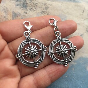 May include: Two silver compass charms with a detailed design. Each charm features a compass rose with the cardinal directions N, S, E, and W.