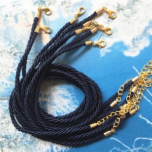 May include: Navy blue braided rope with gold-colored clasps and accents. The rope is tightly woven, and the clasps are attached to the ends. The rope is coiled and ready for use. The background is a light blue and white pattern.