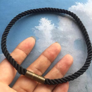 May include: A black braided rope bracelet with a brass clasp.