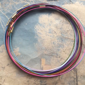 May include: A collection of colorful necklace cords in various shades, including pink, blue, and gold. Each cord is connected with a gold-colored clasp. The cords are arranged in a circular shape, creating a vibrant and eye-catching display.