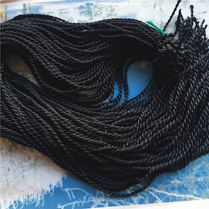 May include: A close-up of a large bundle of black twisted cord. The cord is tightly wound and appears to be made of a soft, pliable material.