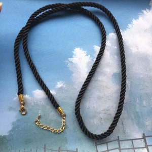 May include: A black cord necklace with a gold clasp and extender chain.