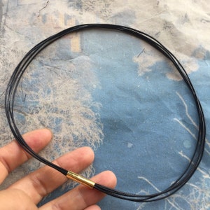 Puede incluir: Un collar negro de múltiples hilos con un cierre dorado.